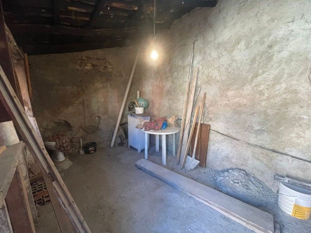Vecchio garage in ristrutturazione, pareti di pietra e pavimento in cemento, strumenti da lavoro e materiali edili presenti, ambientazione per lavori di restauro o ristrutturazione edilizia.