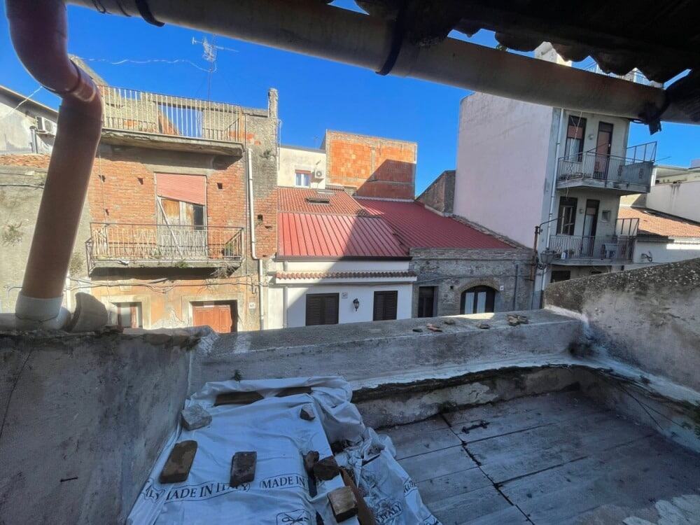 Tetti e balconi di case tradizionali in un vicolo urbano, vista da un balcone di un edificio, con cielo blu e dettagli architettonici, in un contesto di quartiere residenziale storico.