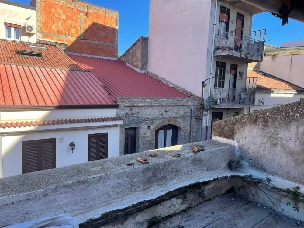 Tetto con copertura in tegole rosse, affaccia su un quartiere residenziale di città storica, con edifici in pietra e balconi in ferro battuto, ideale per ristrutturazione e valorizzazione immobiliare.