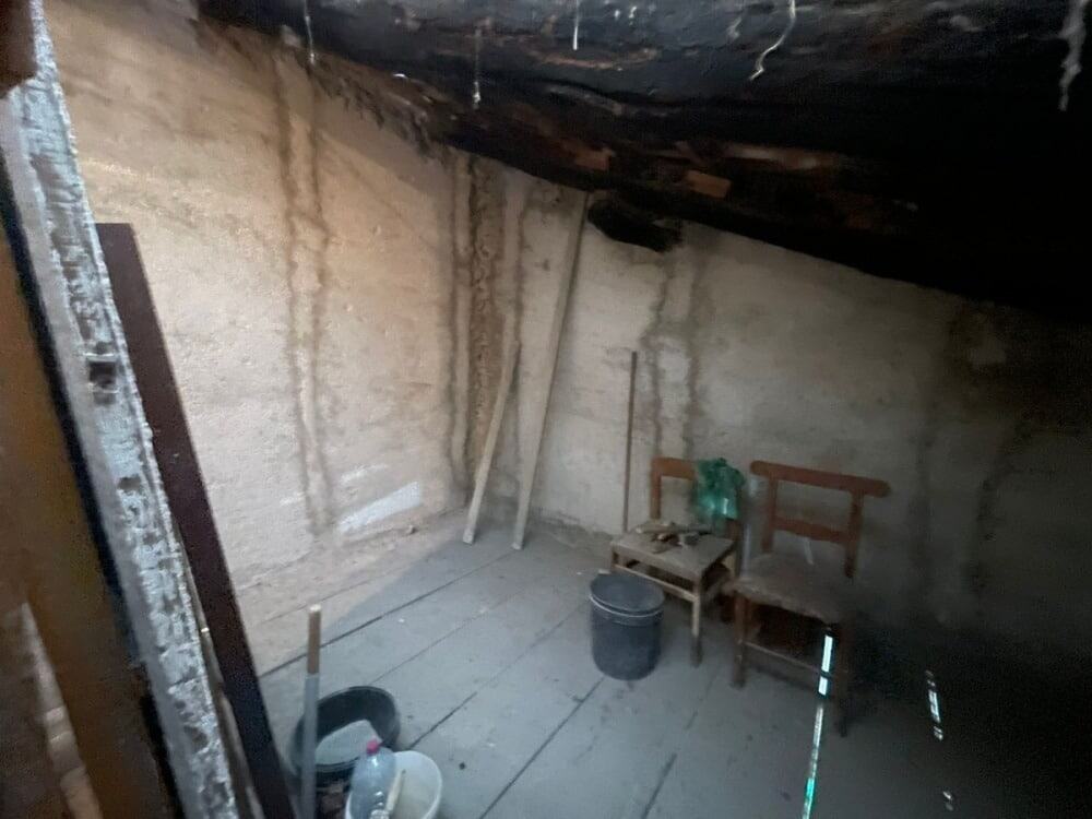 Ripostiglio sottotetto in fase di ristrutturazione, pareti in muratura e soffitto in legno con materiali da lavoro e attrezzi di bricolage. ideale per progetti di ampliamento o arredamento rustico.