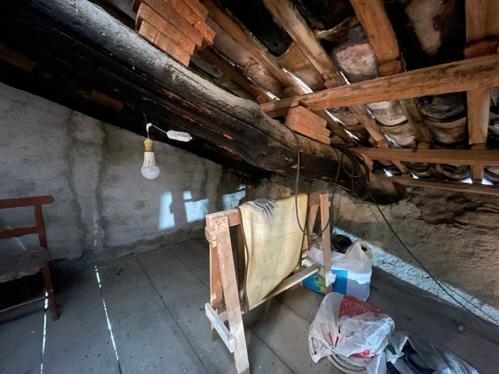 Fornace sottotetto in ristrutturazione con travi in legno, quarzi e materiali edili, ambiente di lavori, illuminazione con lampadina e telai di sostegno, elementi di costruzione storica.