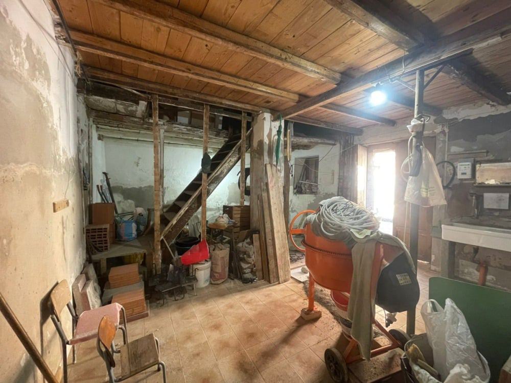 Vecchia casa in ristrutturazione con muro in pietra, attrezzi da lavoro e armature in legno, ambiente da rinnovare, ideale per ristrutturatori e hobbisti, con impianto di illuminazione attivo.