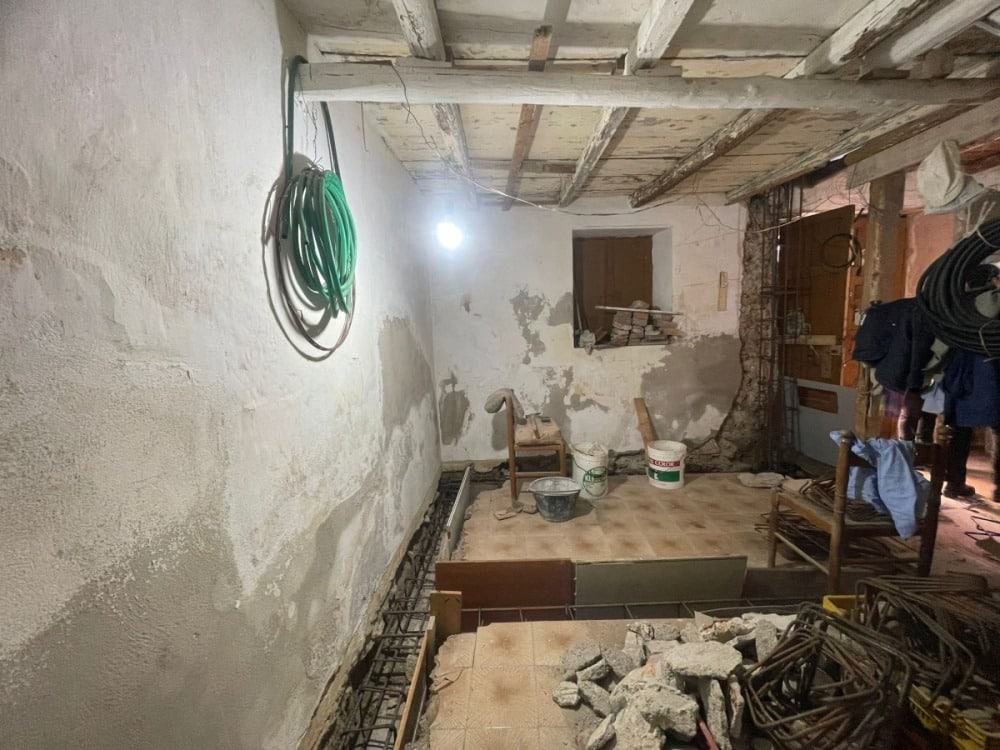 Scavi e ristrutturazione di una stanza in fase di restauro, lavori di muratura, tubature e pavimentazione in corso in un cantiere edile.