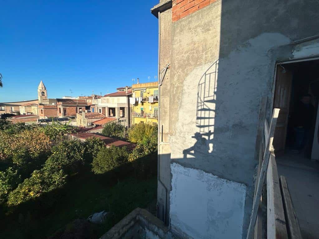 Vista sul centro storico di una città italiana, con edifici tradizionali e una chiesa con torre campanaria, e un balcone in fase di ristrutturazione, con ambiente urbano vivace e patrimonio architettonico.