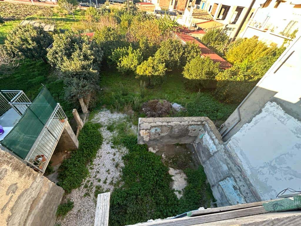 Verde giardino con alberi e siepi, vista dall'alto di un cortile di una casa in fase di ristrutturazione, con spazi verdi e ville circostanti in contesto urbano.