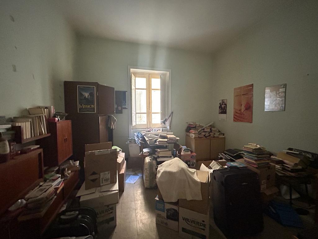 Stanza disordinata con libri, scatole e mobili, ambientazione di una casa da ristrutturare o organizzare.