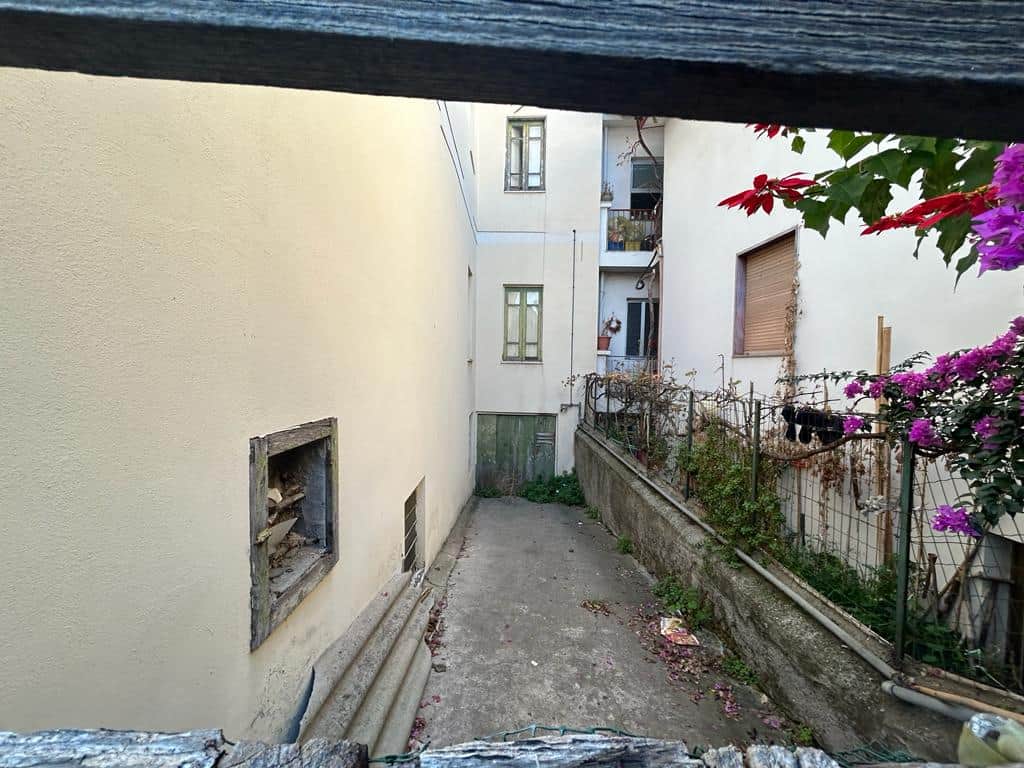 Stanza interna di una casa in stile italiano, con piccolo cortile esterno e piante fiorite, ideale per soluzioni di ristrutturazione e miglioramento abitativo.