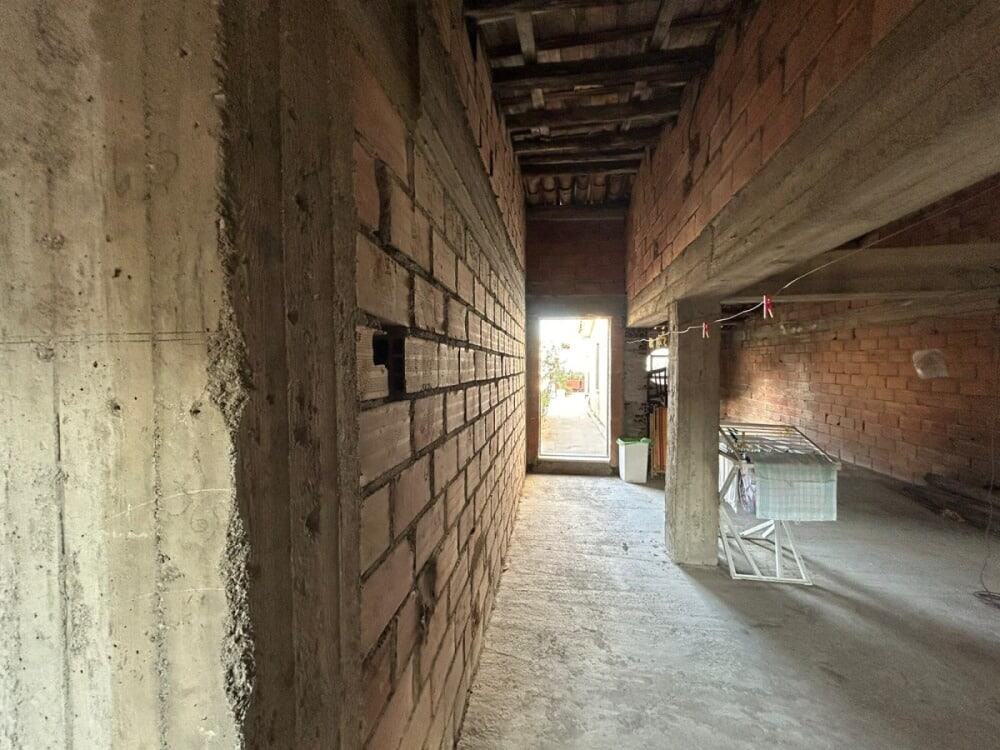 Franzoio di una casa in costruzione con muri in mattoni e sopra un pavimento in cemento, vista verso una porta d'ingresso luminosa.