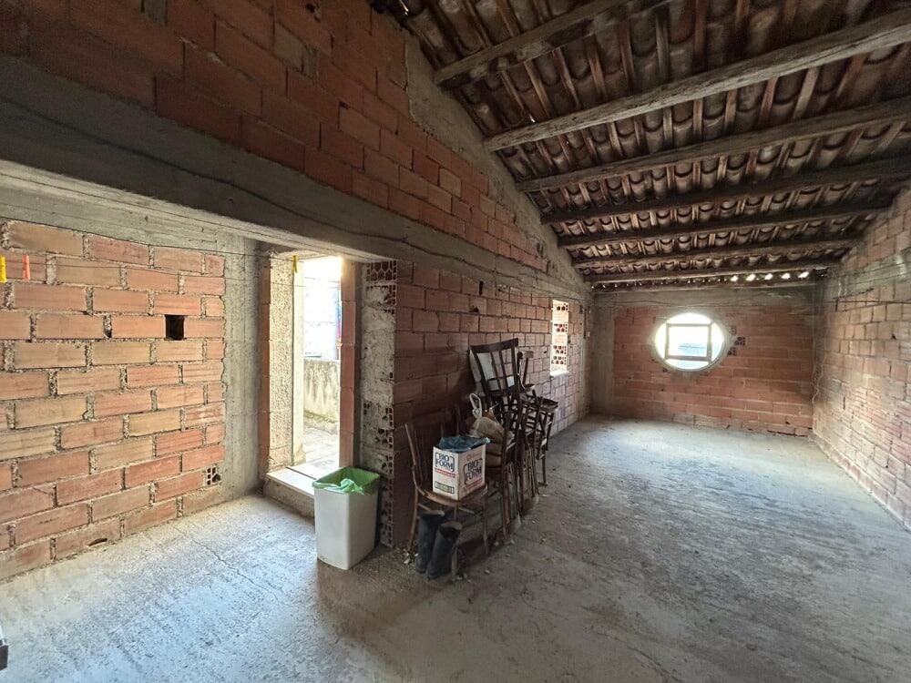 Open space in a rustic unfinished attic with exposed brick walls, wooden beams, and natural light from small windows, ideal for renovation or conversion projects in Italy.