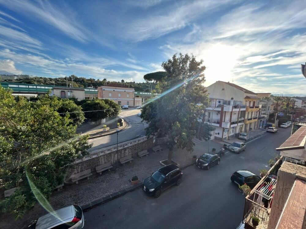 Finestra sulle strade di un quartiere residenziale al tramonto con case, pini e auto parcheggiate, atmosfera tranquilla e panoramica, ideale per promuovere immobili e immobiliari a NextCasa, Milano.