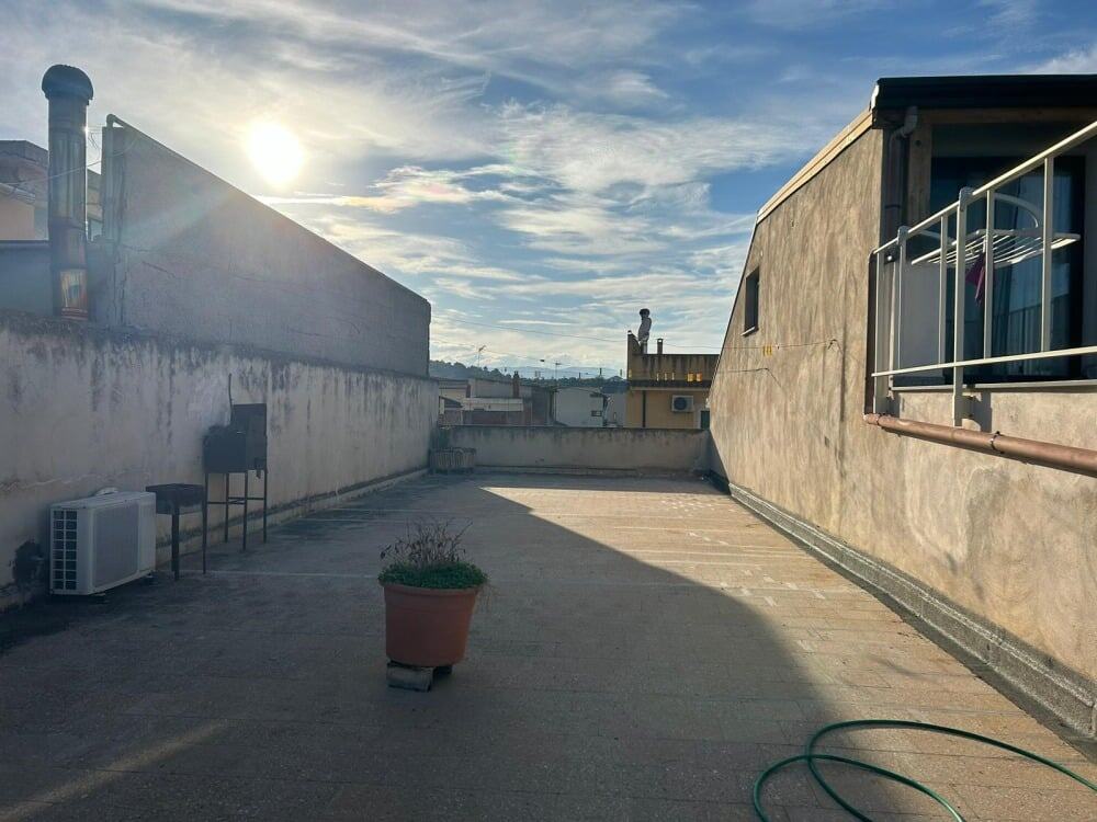 Ampio terrazzo in edilizia urbana con vista sul cielo sereno e alcune strutture di condominio sullo sfondo, ideale per relax e attività all'aperto.