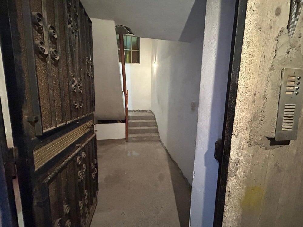Porta d'ingresso in ferro battuto all'ingresso di un edificio, vista dall'esterno, con scala interna e pareti in fase di ristrutturazione, ideale per immobili residenziali o commerciali.