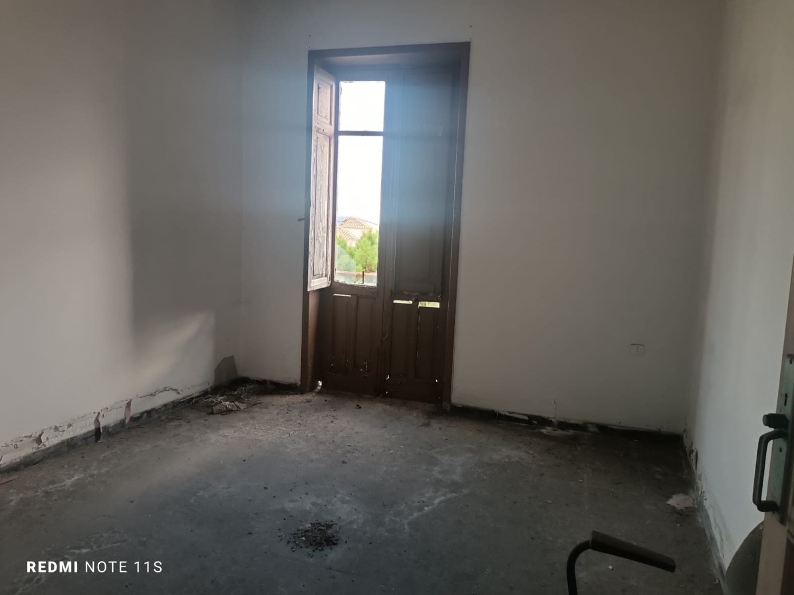 Finestra in una stanza da ristrutturare, pareti bianche, pavimento in cemento, ambiente luminoso, immobile in fase di preparazione per interventi di rinnovo, ideale per investitori o progetti di interior design.