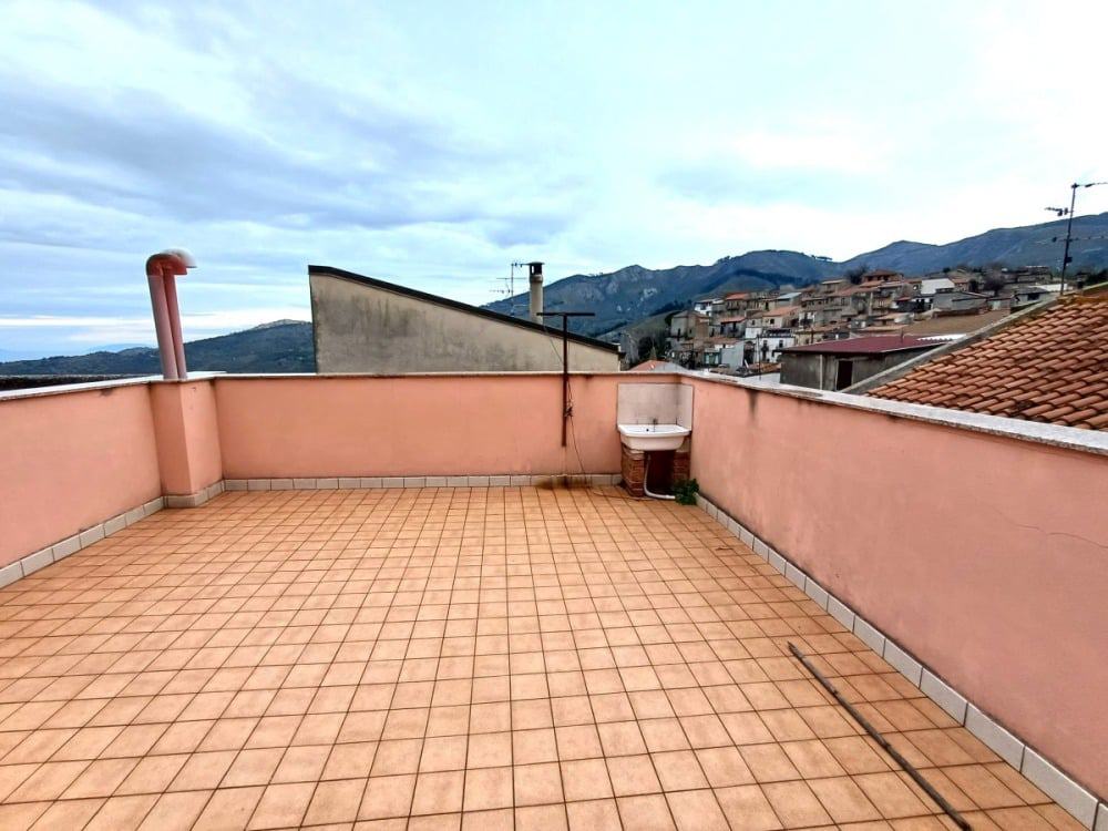 Terrazza panoramica con vista sulle colline e sui tetti delle case. Spazio esterno ideale per relax e convivialità, con pavimentazione in piastrelle e angolo lavabo. Perfetta per appartamenti e case in affitto o vendita.