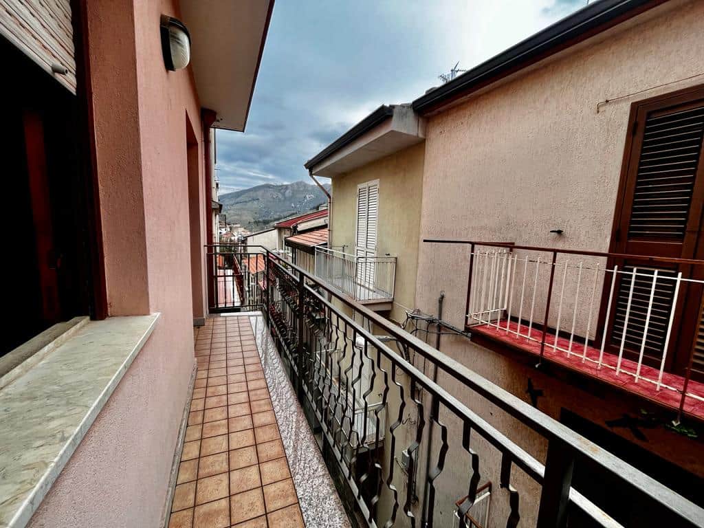 Balcone di appartamento con vista sulle montagne, con ringhiera in ferro battuto e pavimento in piastrelle, in un quartiere residenziale di montagna.