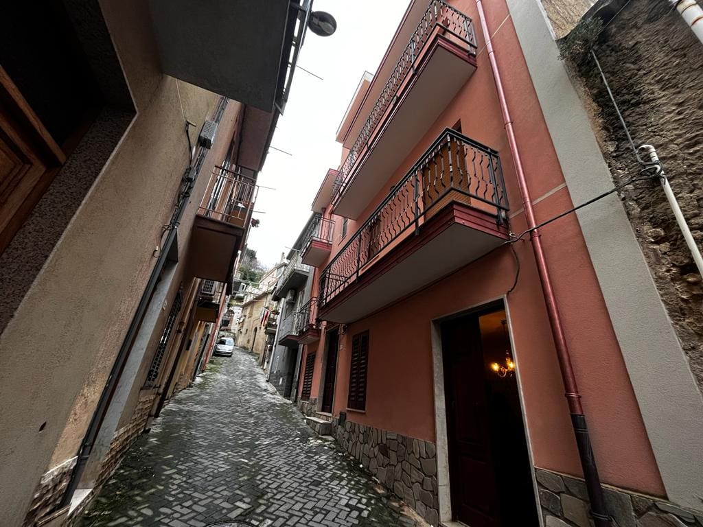Vecchio vicolo di quartiere con case colorata, facciata in pietra e ringhiere in ferro battuto, strada in ciottolato, atmosfera autentica e suggestiva del centro storico.