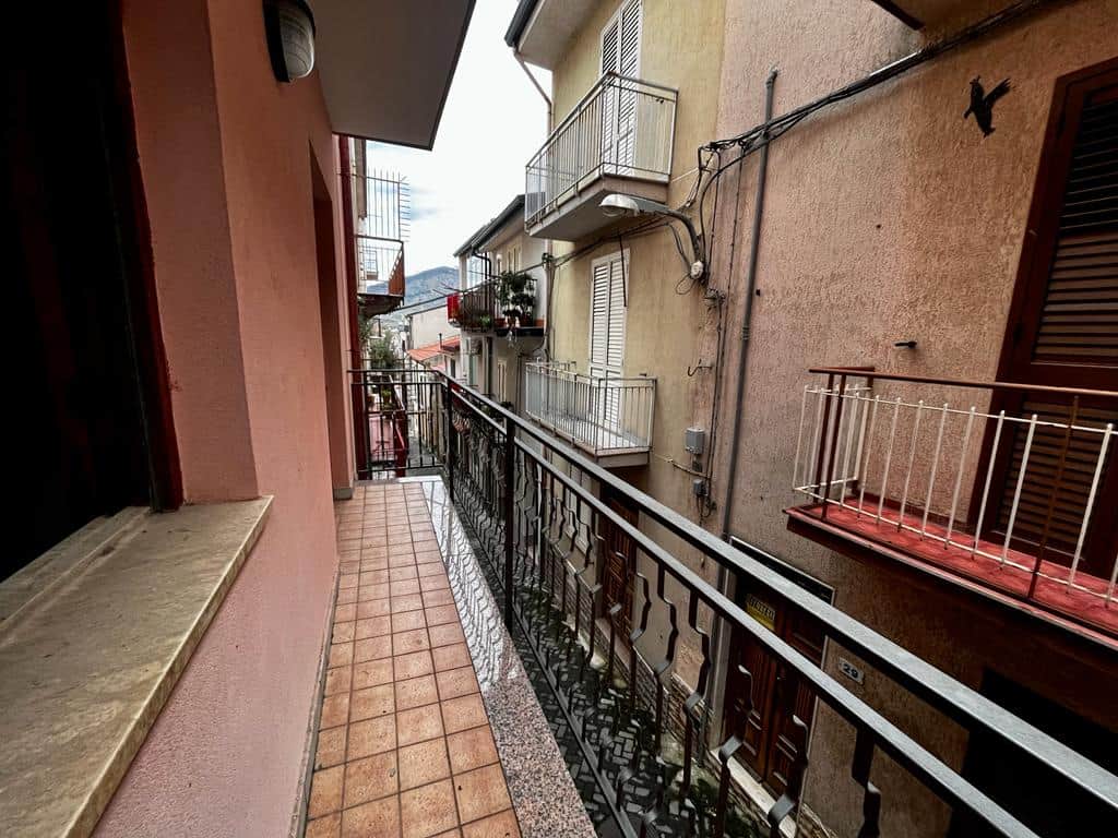 Balcone di un appartamento con ringhiera di ferro battuto, vista sui palazzi vicini e alcune piante sul balcone, in un contesto urbano italiano, immagine luminosa e accogliente.