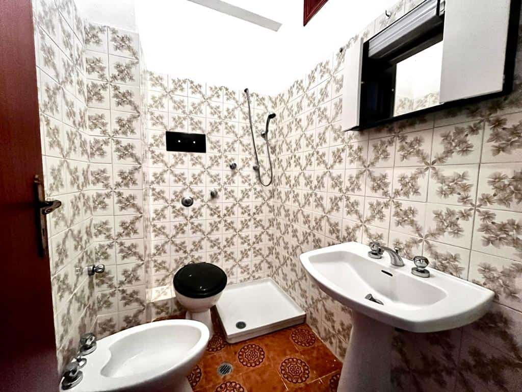 Bagno con piastrelle decorativi, rubinetti e specchio, lavabo e servizi igienici, ambiente piccolo e funzionale, stile vintage, NextCasa immobili in vendita e affitto in Italia.