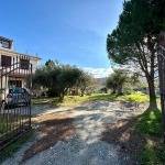 Esito, panoramica di un giardino privato con alberi e spazio verde, ingresso con cancello in ferro battuto, casa residenziale moderna in contesto rurale, atmosfera tranquilla e naturale in Italia.