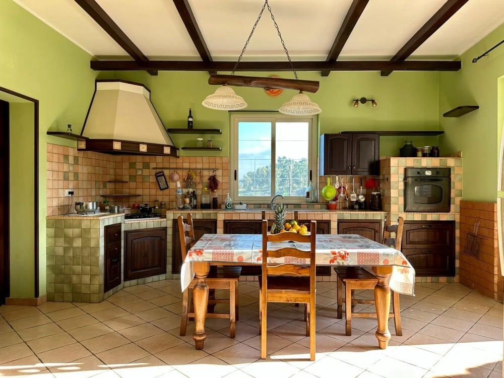 Cucina tradizionale in stile rustico con pareti verde chiaro, mobili in legno scuro e dettagli in ceramica, illuminata da luce naturale, ideale per case vacanza o soggiorni in campagna.