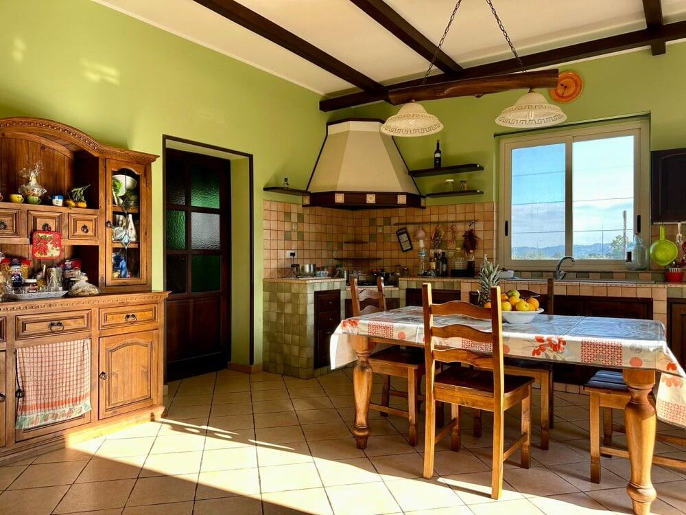 Casetta moderna in stile rustico con cucina abitabile, mobili in legno, pareti verdi e grande finestra che consente l’ingresso di luce naturale. Ideale per vivere in comfort e stile en plein air.