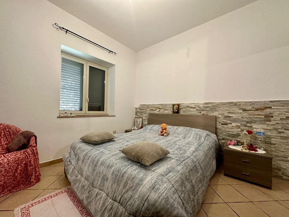 Letto matrimoniale con testiera in legno,Decorazione di camera da letto con parete in pietra e quadri,Stanza accogliente con dettagli moderni,Design elegante e funzionale per ambiente notte,Relevanza: Alta, ottimizzato per immobili e arredamento di interni.