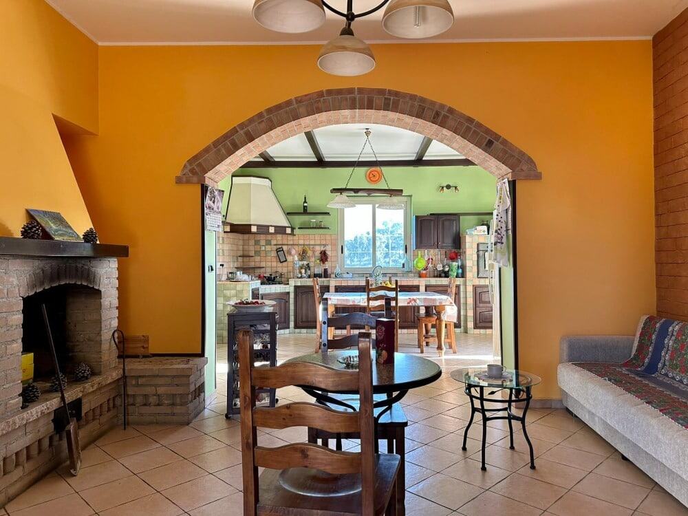 Finestra con cucina colorata in stile country in un accogliente soggiorno open space. Pareti gialle e arancio, camino in mattoni e mobili in legno creano un ambiente caldo e familiare.