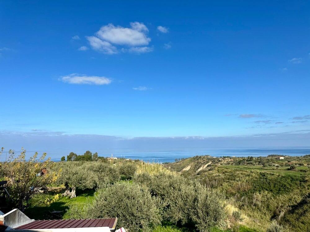 Paesaggio costiero con vista mare, colline verdi e cielo blu in una proprietà immobiliare NextCasa, ideale per investimenti e case vacanze.