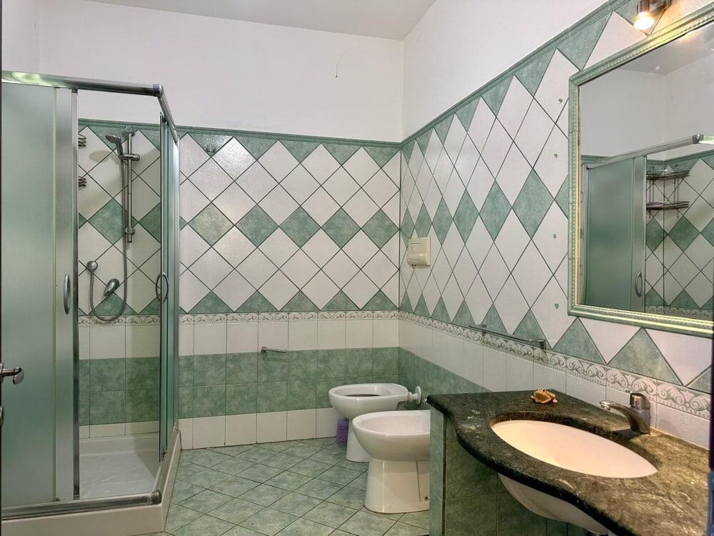 Bagno con doccia, water e lavabo con specchio, piastrelle verde e bianco, dettagli di arredo bagno, ambiente spazioso e luminoso.