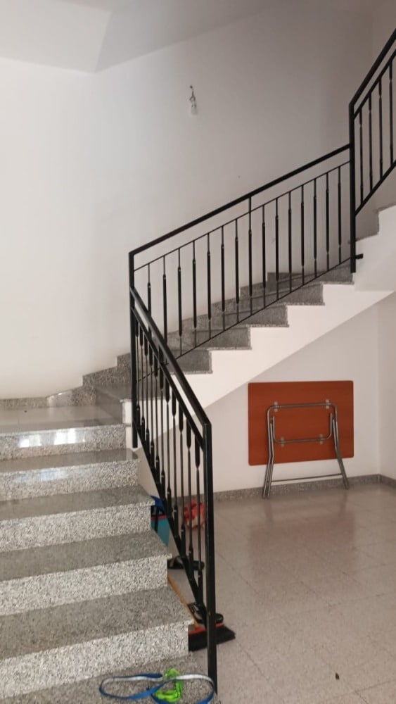 Scale interne in granito con ringhiera in ferro nero, ambiente spazioso e luminoso, ideale per abitazioni e uffici moderni, con dettagli funzionali e stile minimalista.