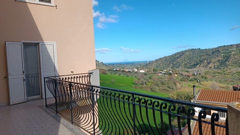 Vista panoramica dal balcone di un appartamento con panorama su colline verdi e mare in lontananza, ideale per case in affitto o vendita a NextCasa.