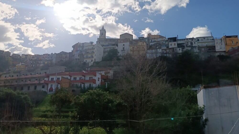 Ville storiche di Napoli con case colorate e chiesa sulla collina, cielo nuvoloso, paesaggio urbano e natura, immagine di città italiana tipica, perfetta per annunci immobiliari NextCasa.