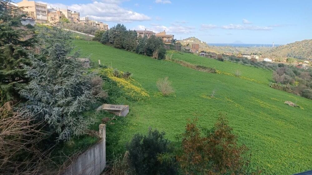 Prato verdeggiante con case sullo sfondo, paesaggio naturale e vista panoramica, ideale per immobili in vendita o affitto, rappresentativo di aree rurali e residenziali in alta qualità.