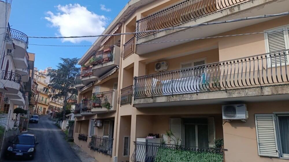 7c76dd75-64d4-4dac-a9b3-5efbebaacae5 Balconi di un edificio residenziale con ringhiere in ferro battuto, aria condizionata e piante sul balcone, in un quartiere urbano.