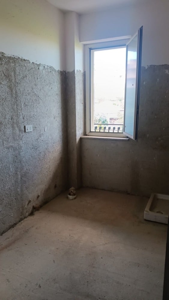 Appartamento in ristrutturazione con pareti in fase di finitura e finestra aperta, pronto per essere arredato.