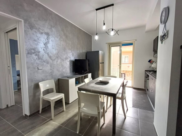 Cucina moderna con sala da pranzo, elettrodomestici, finestra che dà sul balcone, arredamento contemporaneo, illuminazione a sospensione, pavimento in piastrelle gres, stile minimalista, spazio abitativo luminoso, dettaglio di interior design, soluzione residenziale NextCasa.