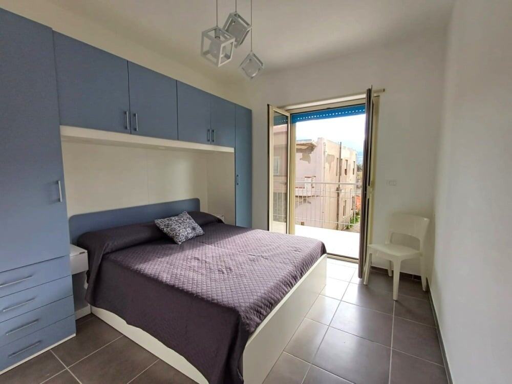 Camera da letto moderna con armadio a muro su misura, grande finestra con vista città, arredi eleganti e atmosfera luminosa, ideale per appartamenti eleganti e funzionali NextCasa.