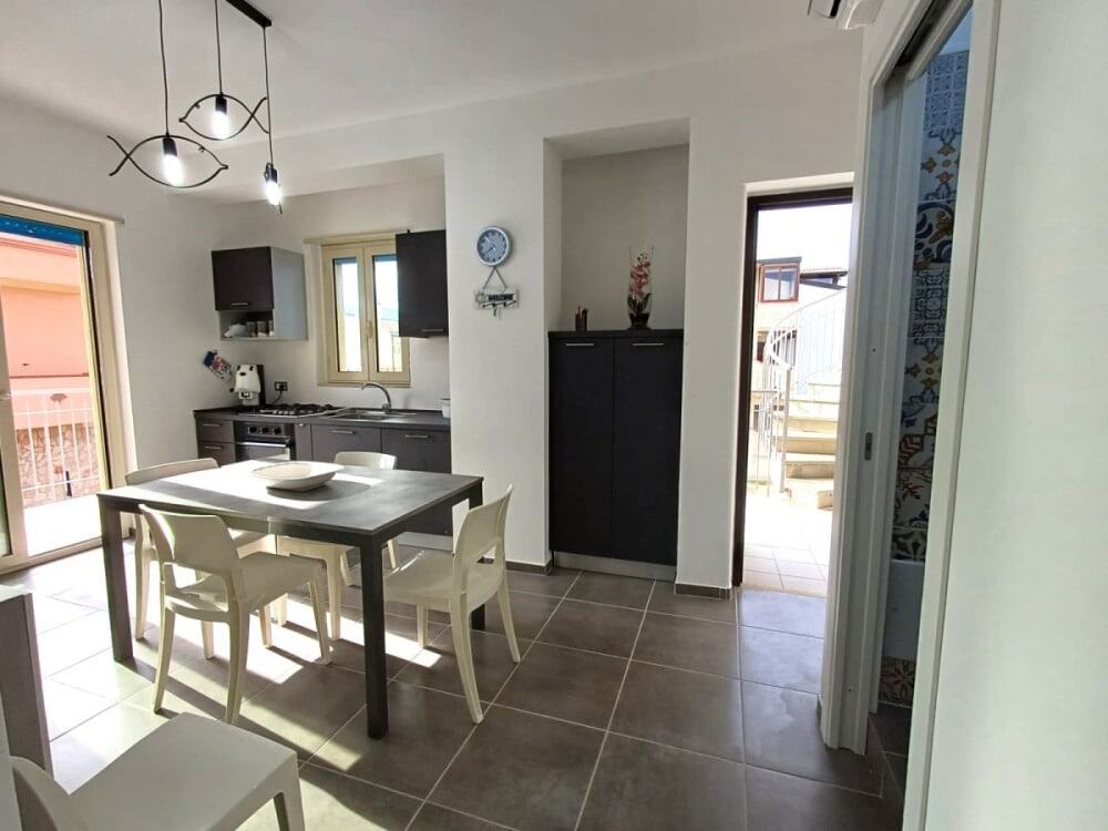 Uisine moderna con accessori bianco e nero, grande tavolo da pranzo, luce naturale, porte scorrevoli, arredamento funzionale, ambientazione di casa vacanze NextCasa, interior design semplice ed elegante.