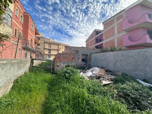Spazio urbano lotto edificabile in zona residenziale con giardino incolto e costruzioni in fase di ristrutturazione o abbandono, perhaps in zona periferica.