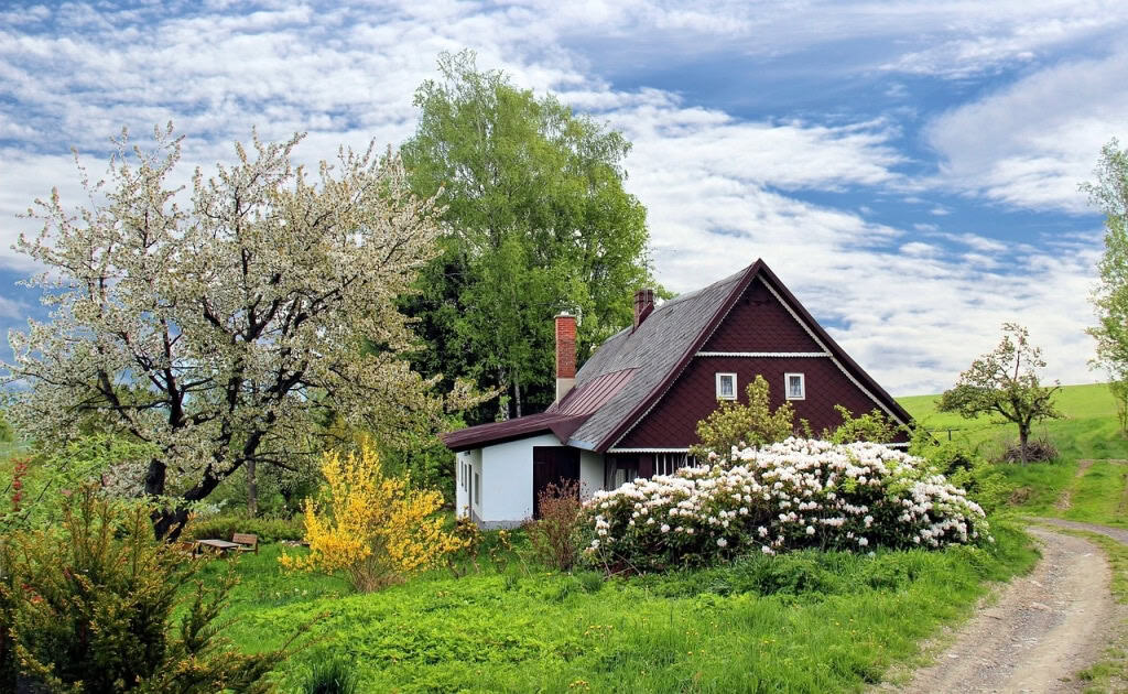 Villa rustica in campagna con giardino fiorito e alberi in fiore, vicino a un sentiero di campagna. Ideale per case di vacanza o residenze in stile tradizionale con ampi spazi verdi.