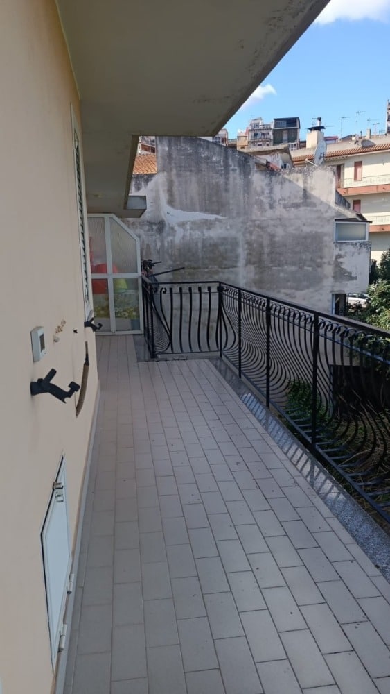 Balcone di un appartamento in zona urbana con vista su edifici circostanti, pavimentato e con ringhiera in ferro nero, ideale per relax e vita all'aperto.