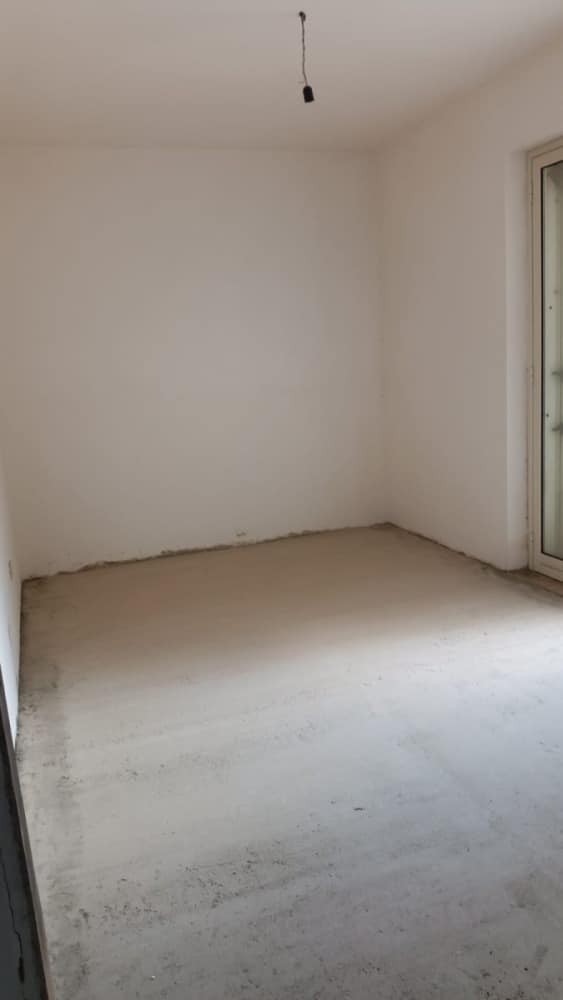 Stanza in corso di ristrutturazione con pareti bianche e pavimento ancora da finire, pronta per essere arredamento.