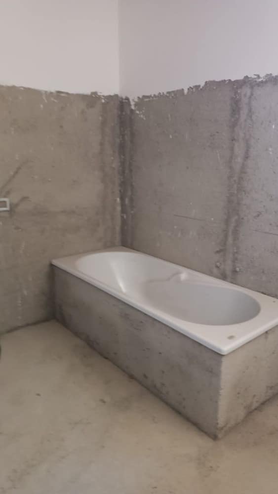 Vasca da bagno in fase di installazione in un bagno in costruzione, con pareti in cemento grezzo e pavimento in completamento lavori.