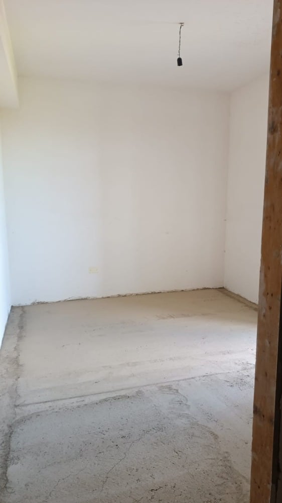Paredi e pavimento di una stanza in fase di ristrutturazione, pronti per essere rifiniti, con pareti bianche e pavimentazione in cemento grezzo.