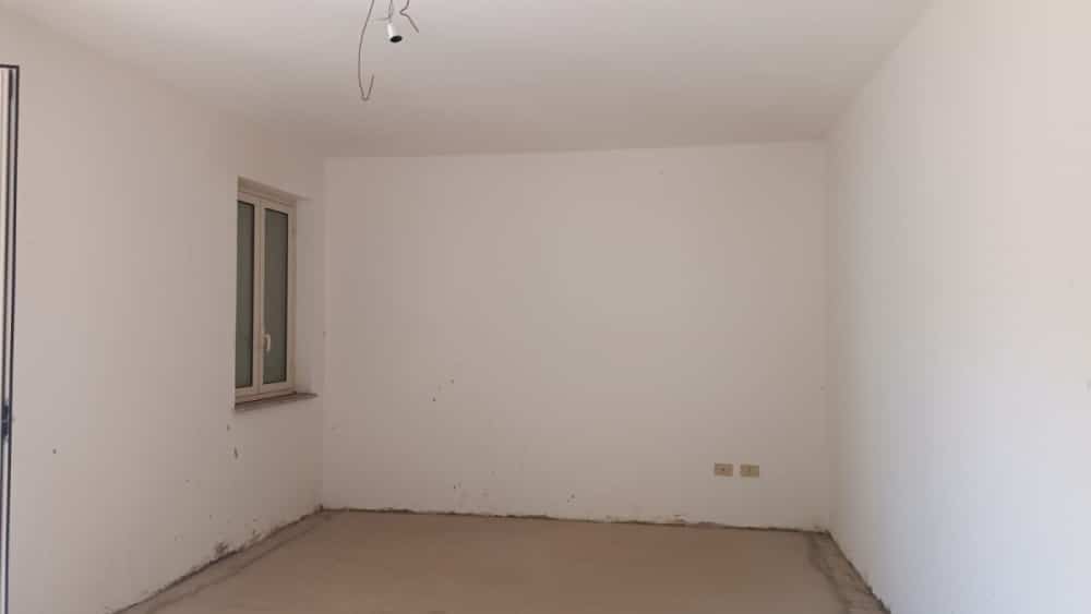 Nuova casa da ristrutturare con pareti bianche e pavimento in fase di completamento, grande finestra per illuminazione naturale, ideale per progetti di interior design moderni.
