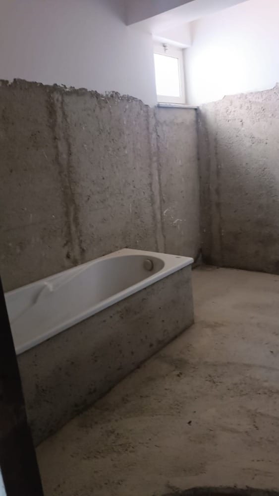 Bagno in fase di ristrutturazione con pareti in cemento grezzo e vasca moderna installata, spazio luminoso con finestra naturale.