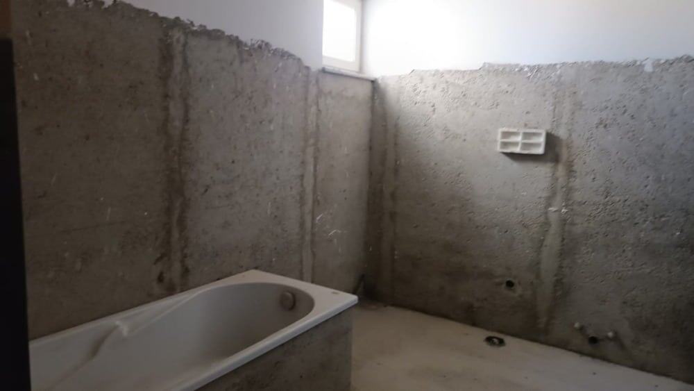 Immagine di una stanza in fase di ristrutturazione con pareti in cemento grezzo, un'installazione di una vasca da bagno e impianti idraulici in vista, pronta per trasformarsi in un bagno moderno e funzionale.