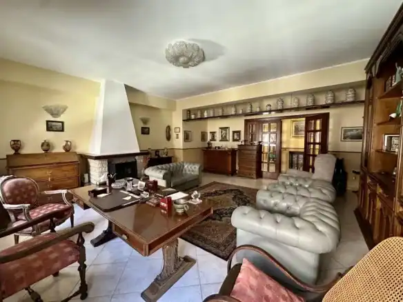 Soggiorno spazioso e elegante con mobili classici, camino in pietra, divani in pelle e dettagli decorativi in stile tradizionale, ideale per momenti di relax e convivialità.