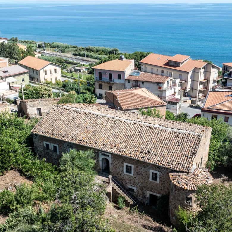Elegante casa storica in pietra con vista panoramica sul mare, circondata da vegetazione lussureggiante e vicina alla costa, ideale per residenza o investimento immobiliare in zona esclusiva.