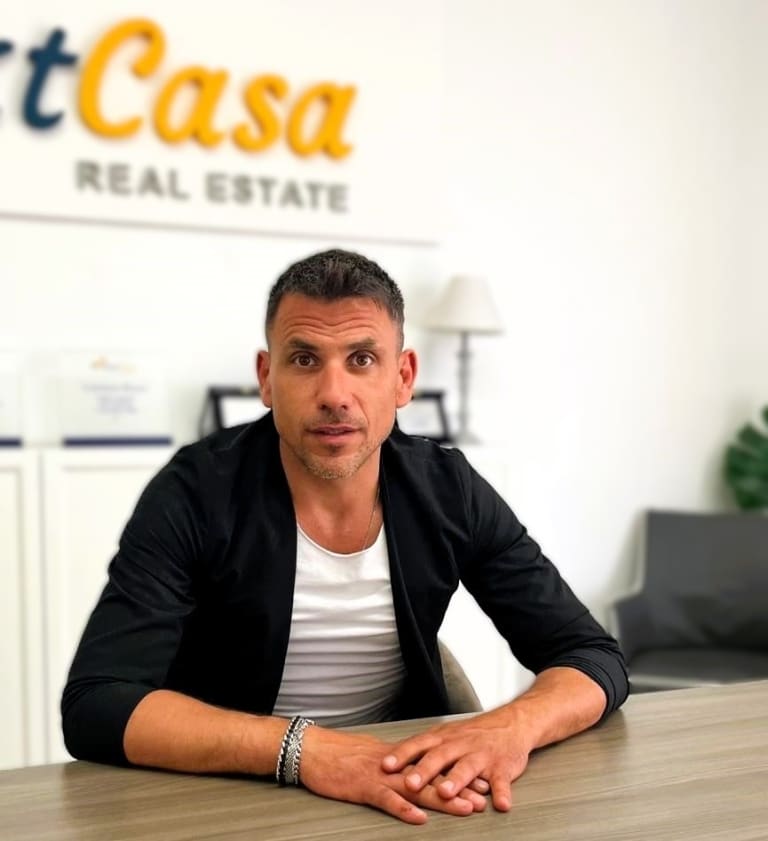 Garante immobiliare professionale in ufficio NextCasa Real Estate con logo sullo sfondo.